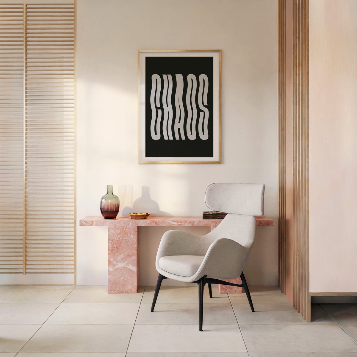Wavy light grey CHAOS lettering on black print shown in a gold frame above a pink marble console and armchair