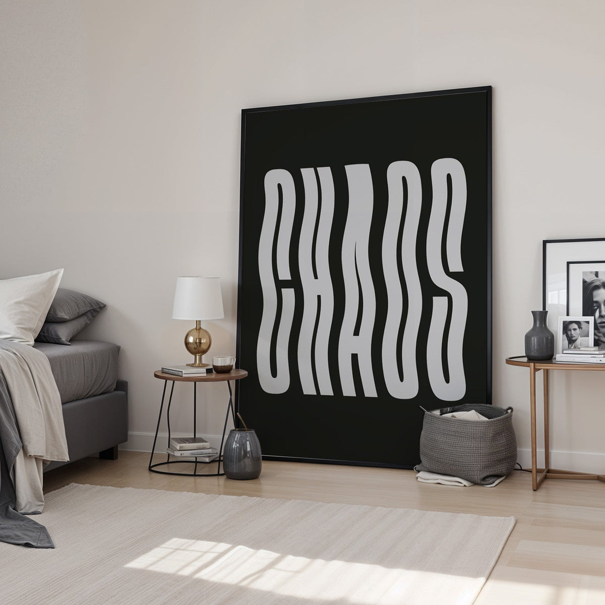 Wavy light grey CHAOS lettering on black print in a black frame leaning in a bedroom beside a gold lamp