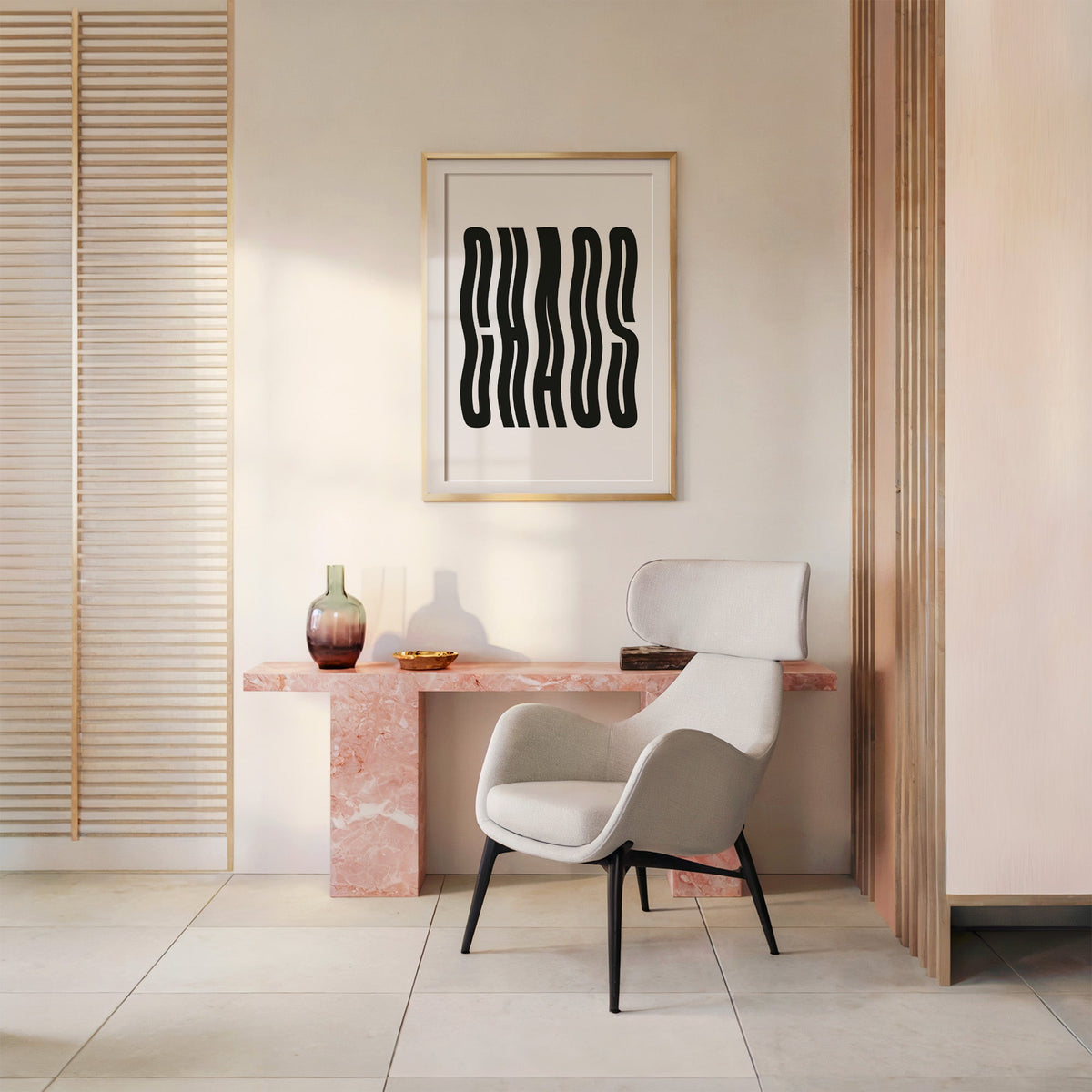 Wavy black CHAOS lettering on white print shown in a gold frame above a pink marble console and armchair