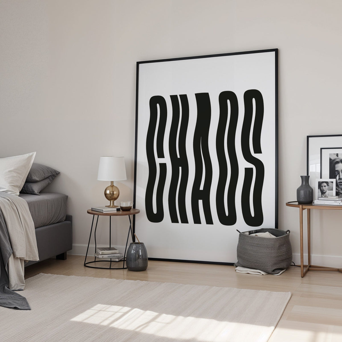 Wavy black CHAOS lettering on white print in a black frame leaning in a bedroom beside a gold lamp
