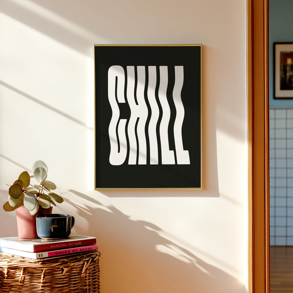 Wavy white CHILL lettering on black print shown in a gold frame above a wicker basket and stacked books