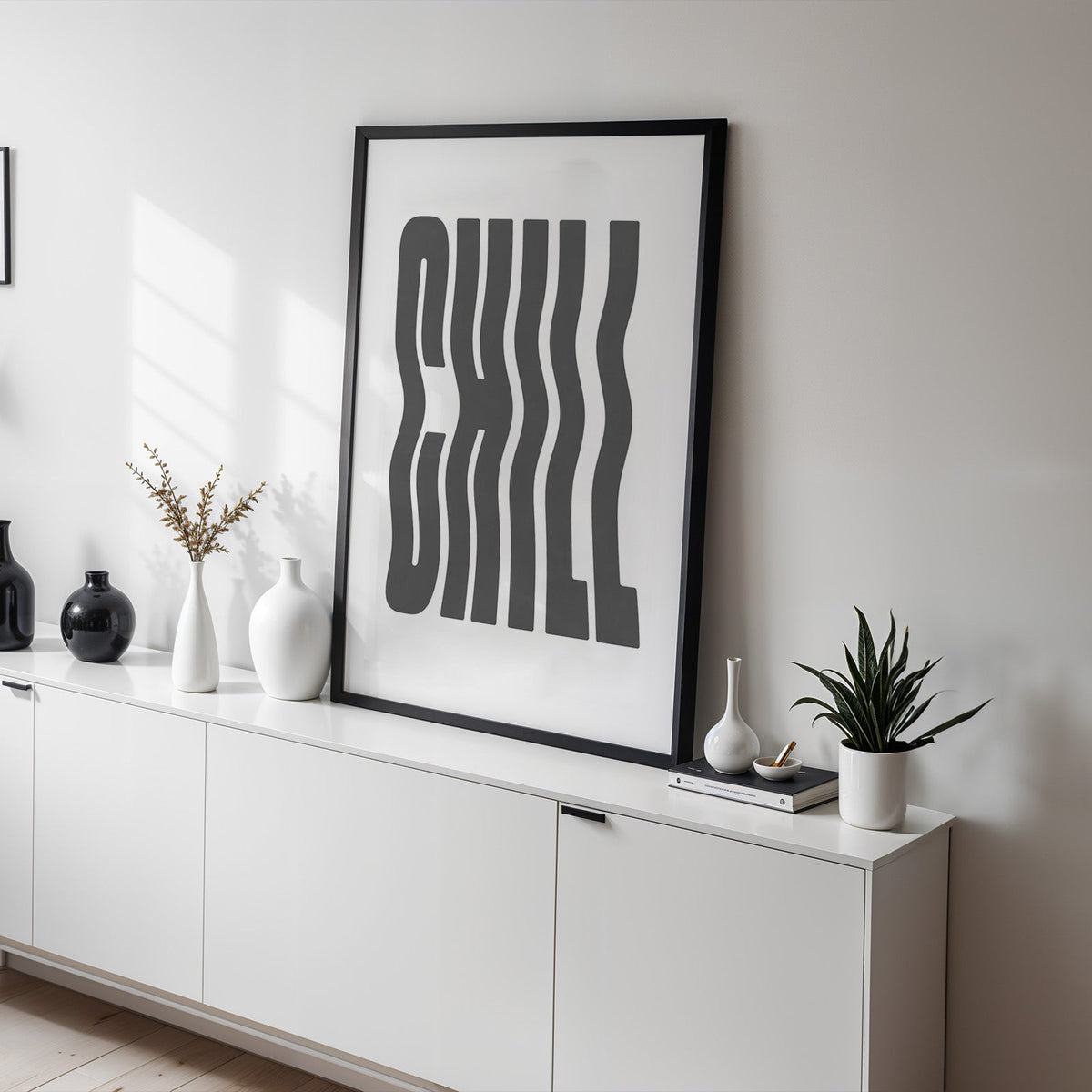 Wavy CHILL lettering on white print in a black frame on a white sideboard with black and white vases
