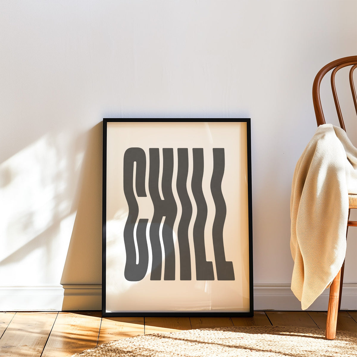 Wavy CHILL lettering on white print in a black frame leaning on a wood floor beside a bentwood chair