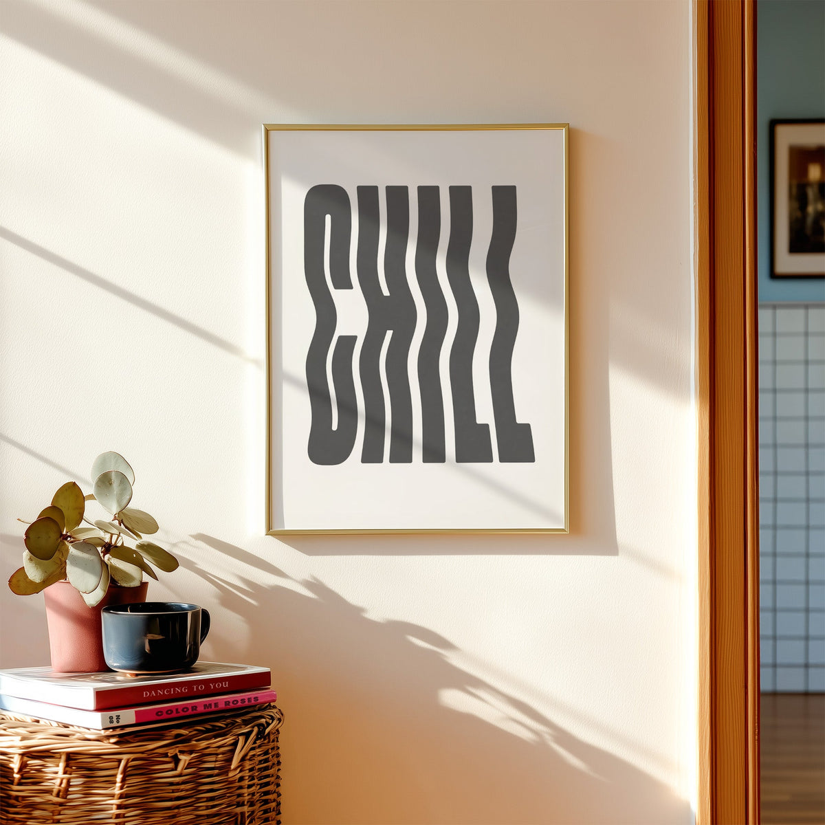 Wavy CHILL lettering on white print shown in a gold frame above a wicker basket and stacked books