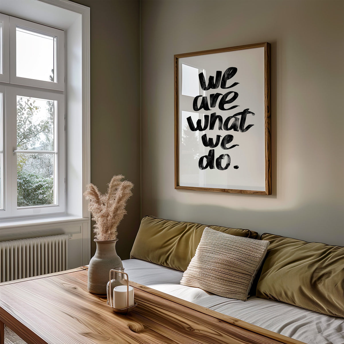 We are what we do brush lettering quote print in a walnut frame above an olive daybed by a window