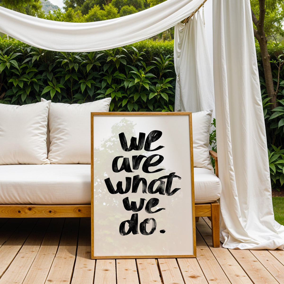 We are what we do brush lettering quote print in an oak frame on an outdoor daybed under white drapes