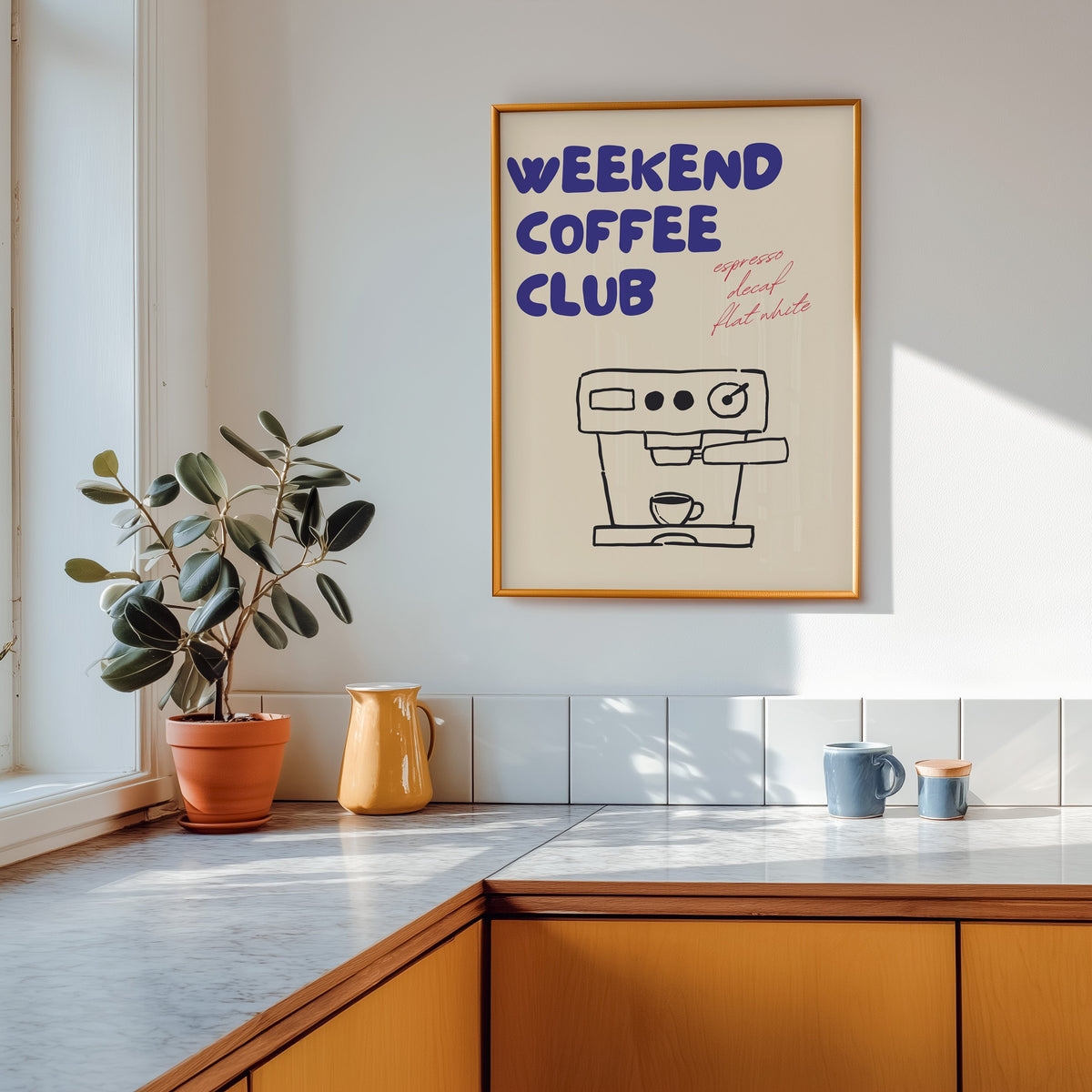 Weekend Coffee Club print shown in a gold frame above a marble counter in a tan kitchen