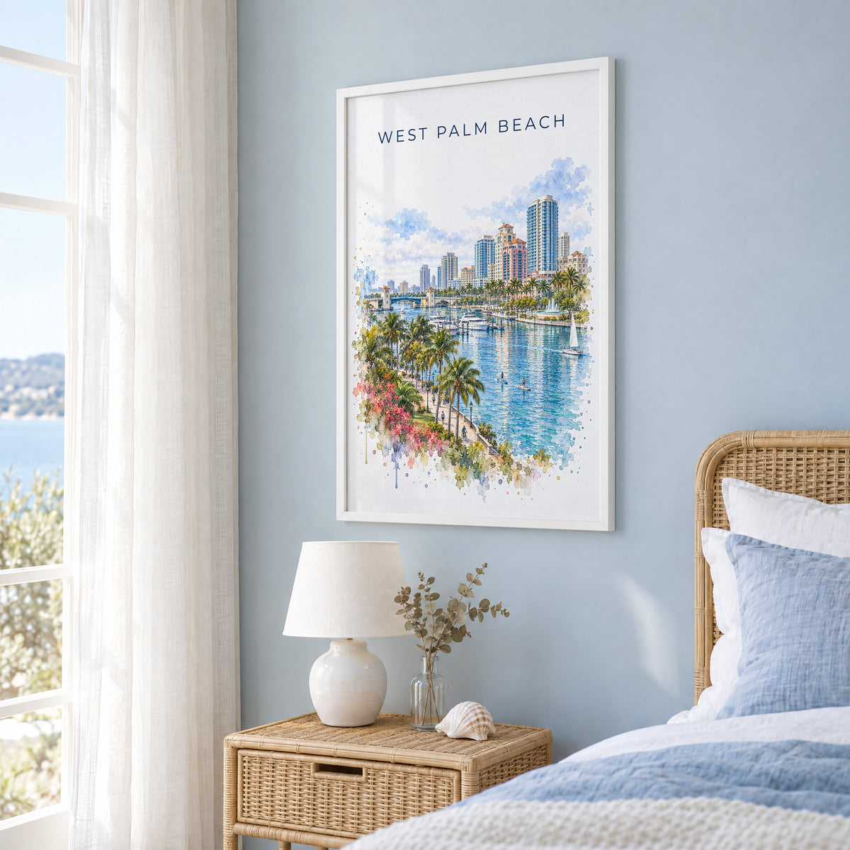 West Palm Beach watercolor print in a white frame on a pale blue wall beside a rattan bed in a coastal bedroom
