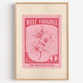 West Virginia state flower stamp print in crimson on pink, light oak frame on a plain white wall