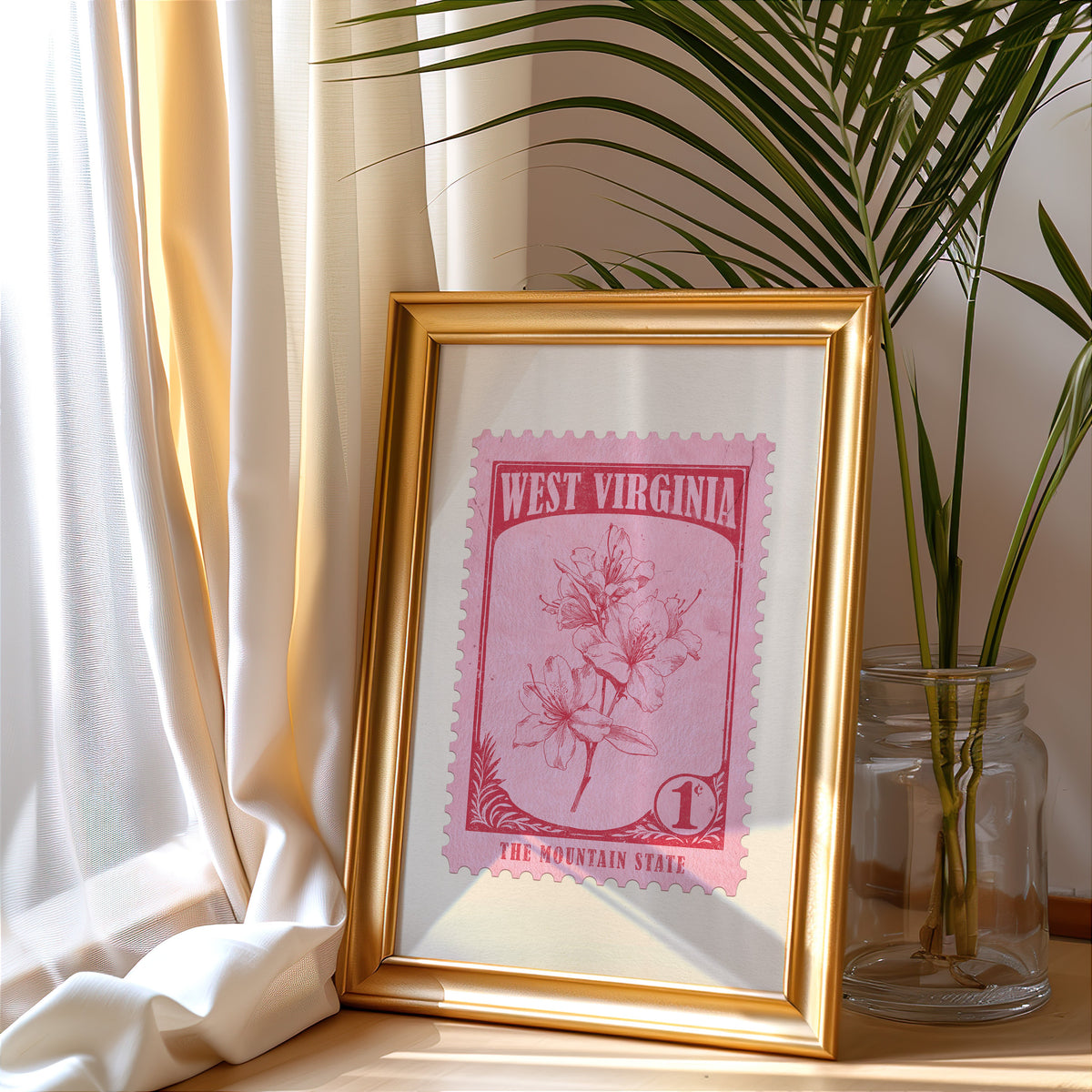 West Virginia stamp print in a gold frame leaning by a cream curtain with a palm in a glass jar