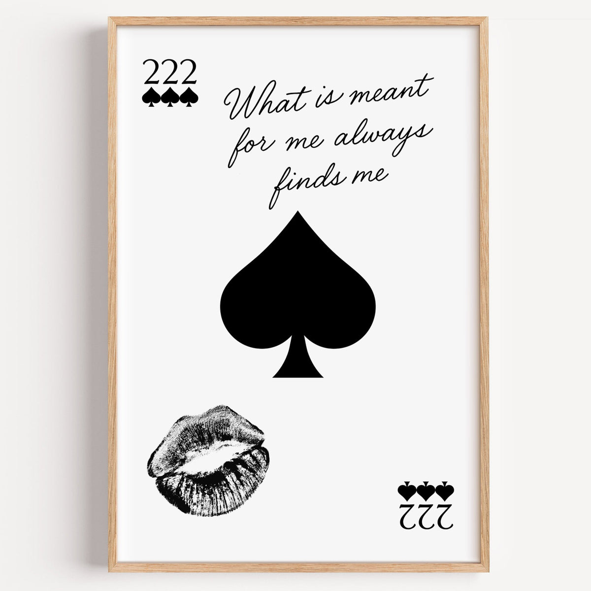Spade, kiss mark and script quote print in a light oak frame on a plain white wall