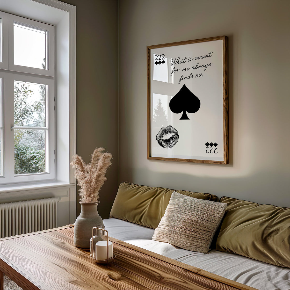 Spade, kiss mark and script quote print in a walnut frame above an olive daybed by a window
