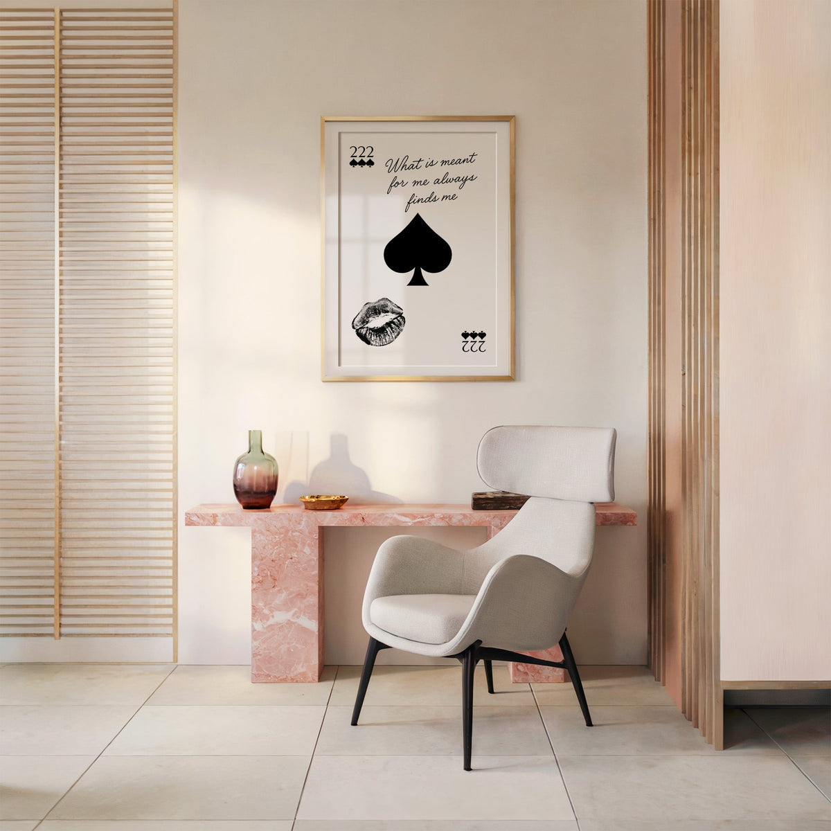 Spade, kiss mark and script quote print shown in a gold frame above a pink marble console and armchair