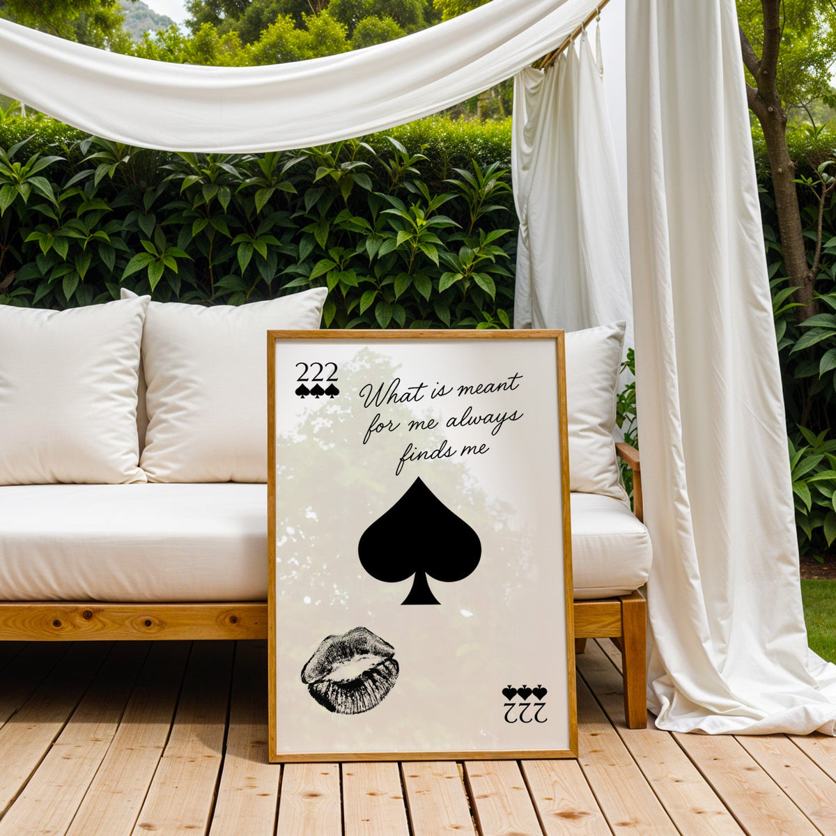 Spade, kiss mark and script quote print in an oak frame on an outdoor daybed under white drapes