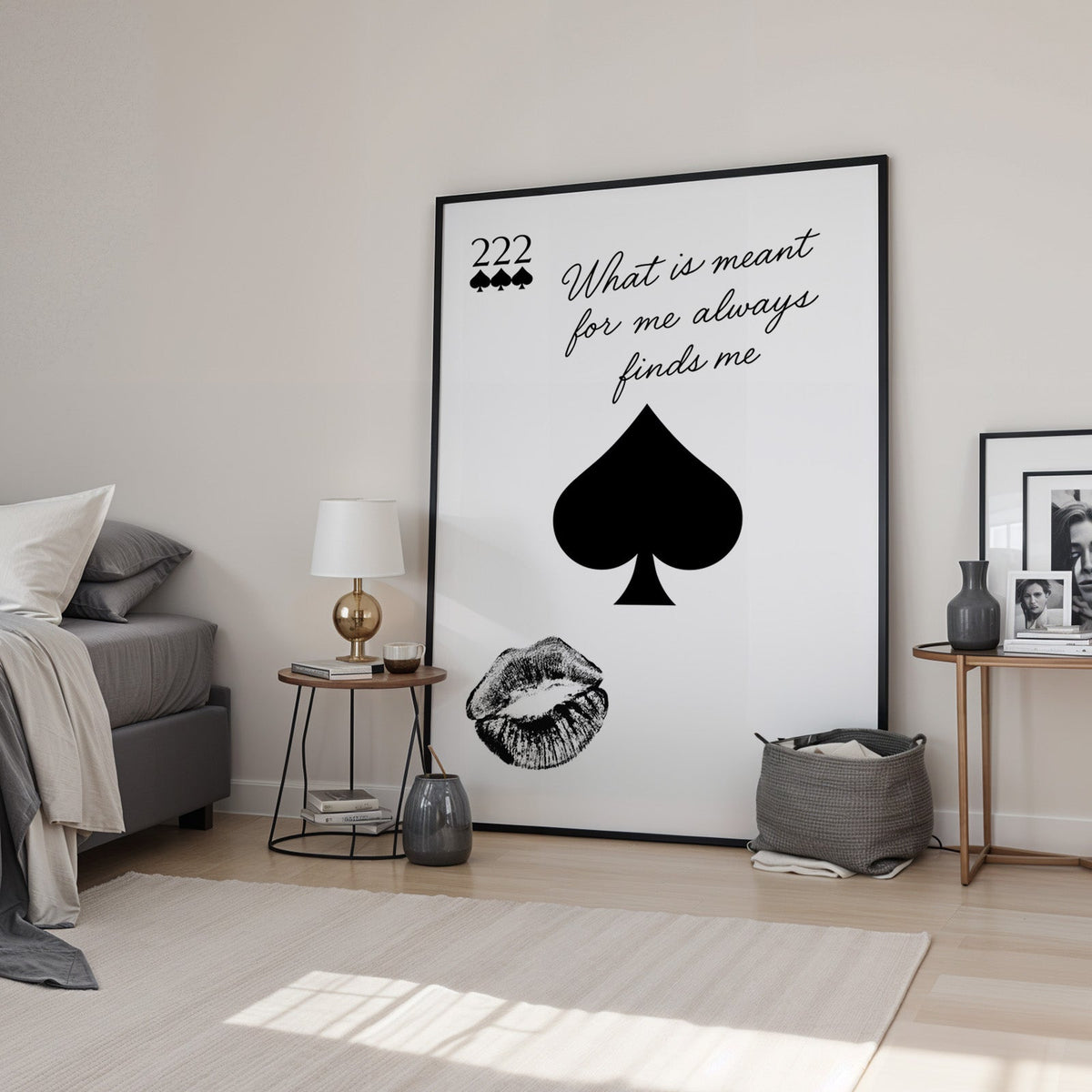 Spade, kiss mark and script quote print in a black frame leaning in a bedroom beside a gold lamp