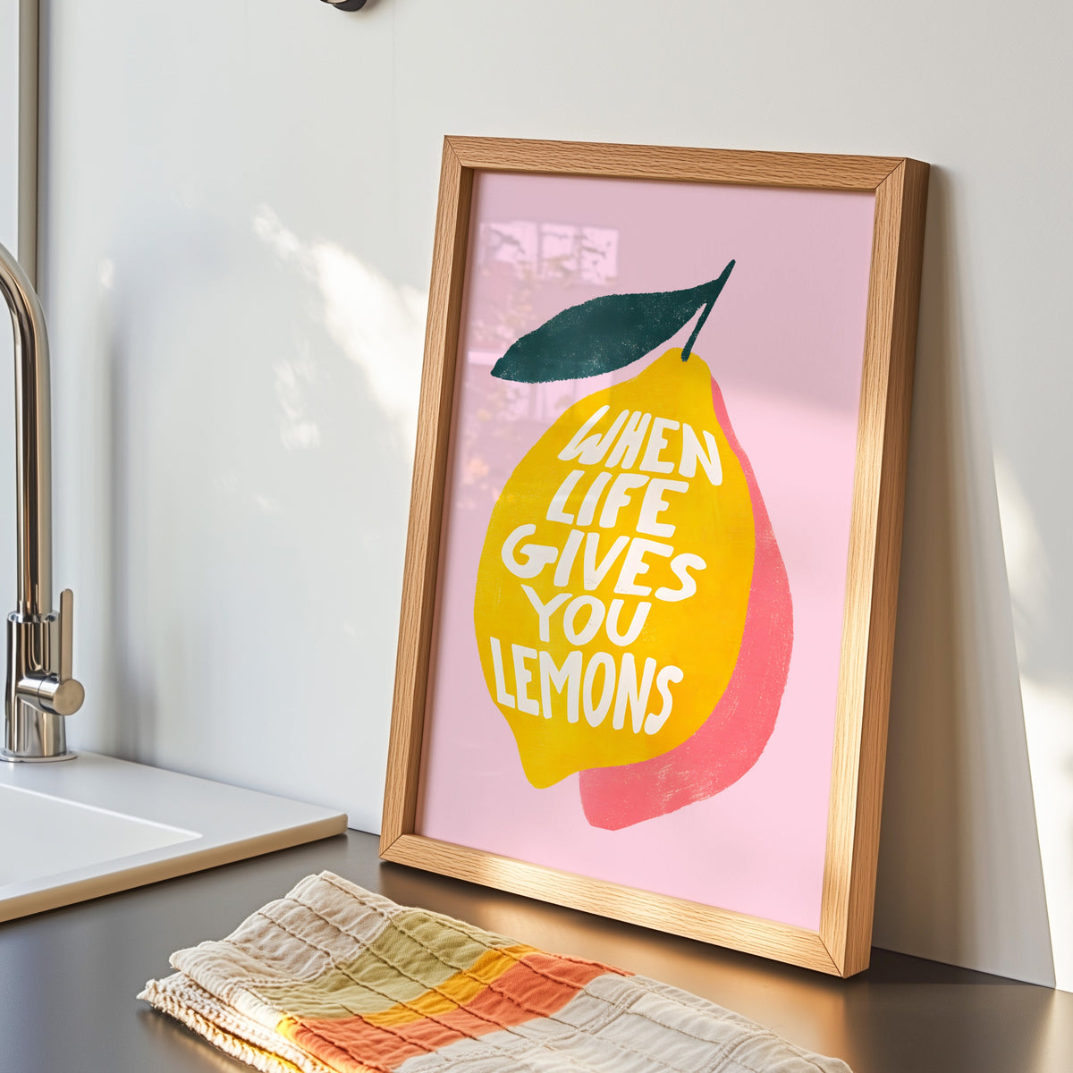 Lemon quote print in an oak frame by the kitchen sink beside a striped tea towel