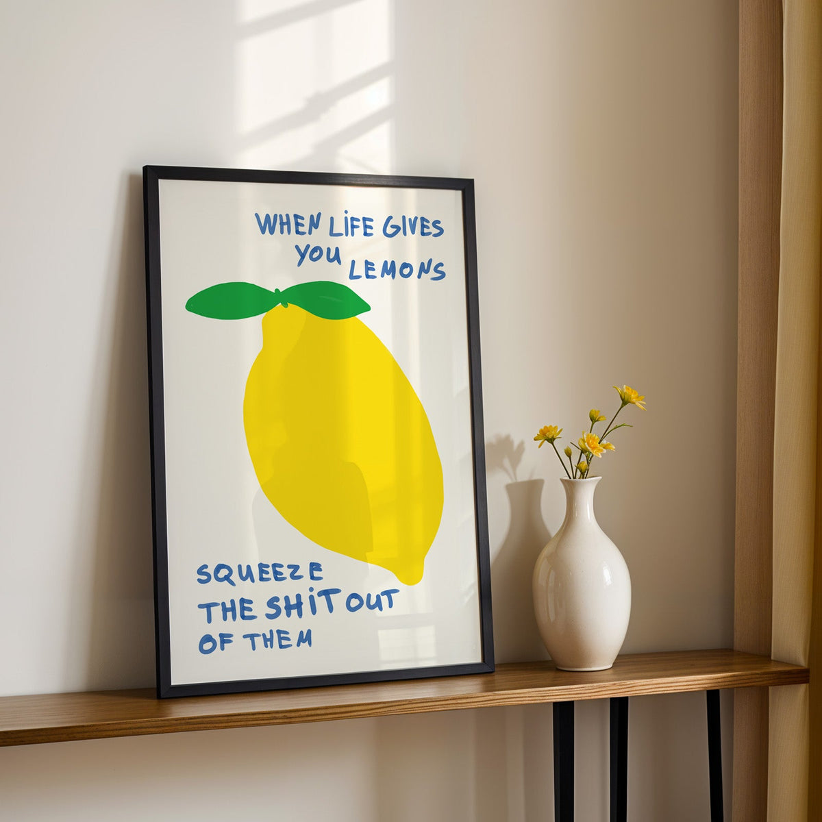 When life gives you lemons print in a black frame on a console table with daisies