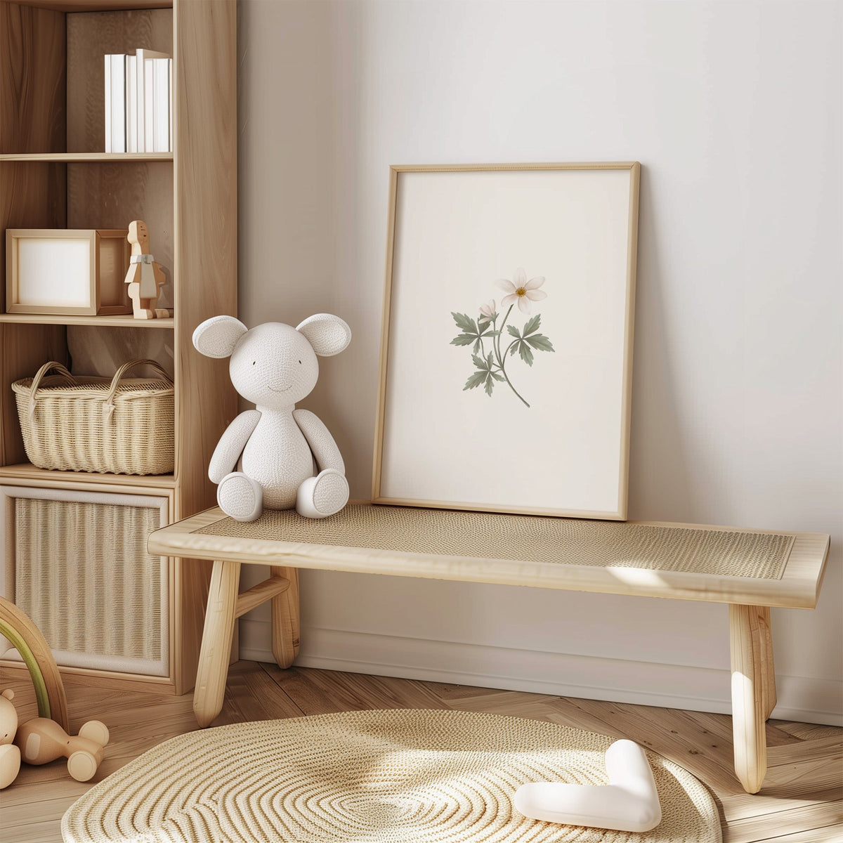 White anemone-style wildflower sprig nursery print in an oak frame on a cane bench beside a white knit plush