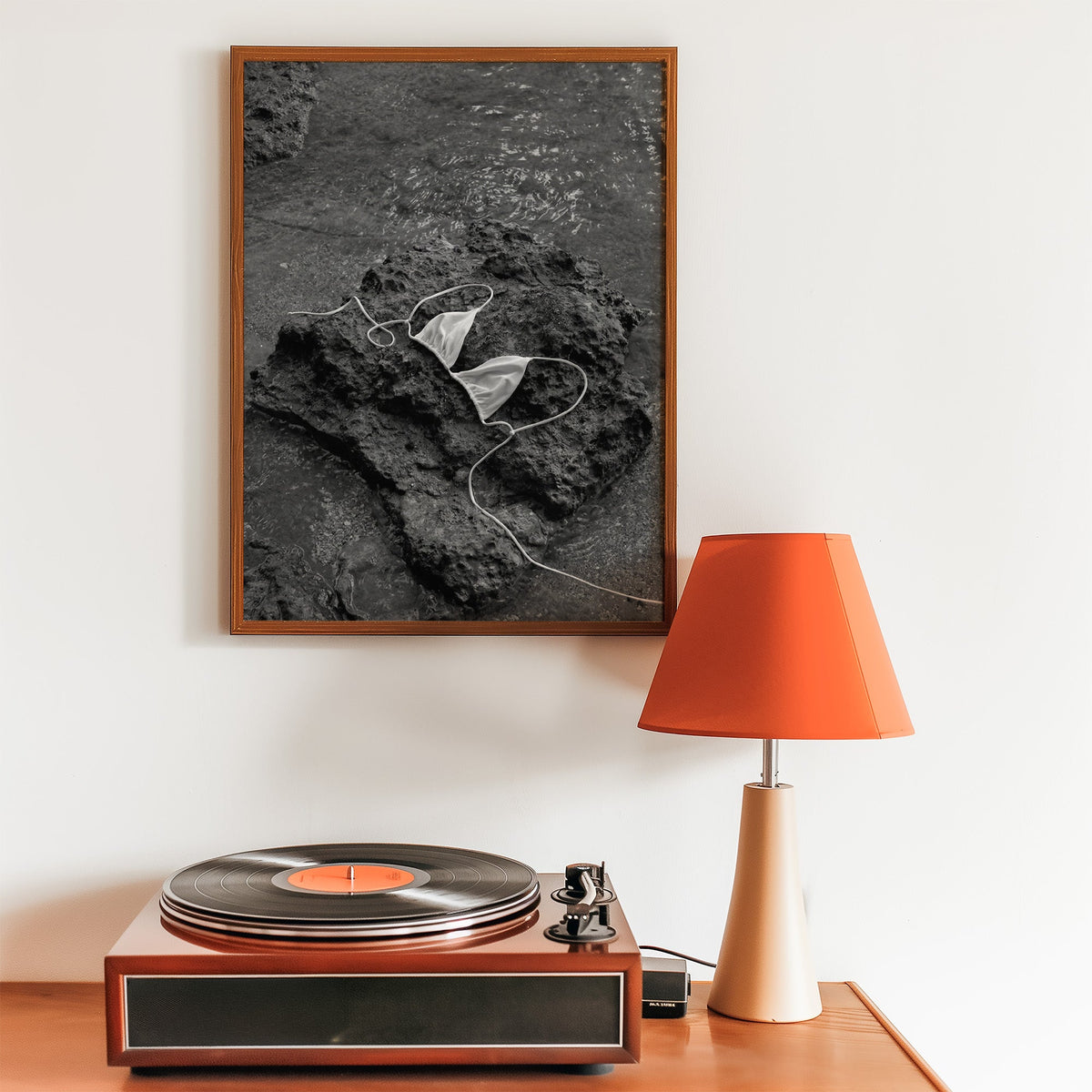 White bikini top on dark volcanic rock print in a walnut frame above a record player and orange lamp
