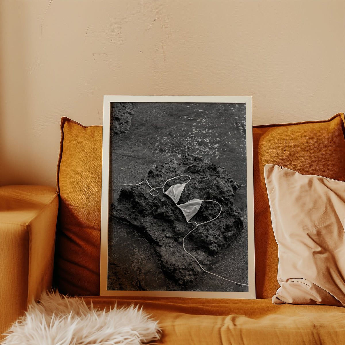 White bikini top on dark volcanic rock print in a white frame leaning on a mustard velvet sofa