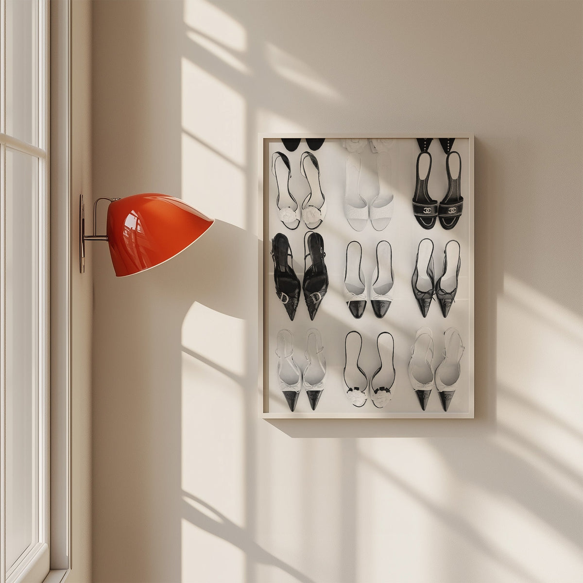 Nine pairs of mules and slingbacks in a grid print in a white frame on a sunlit wall beside a red sconce