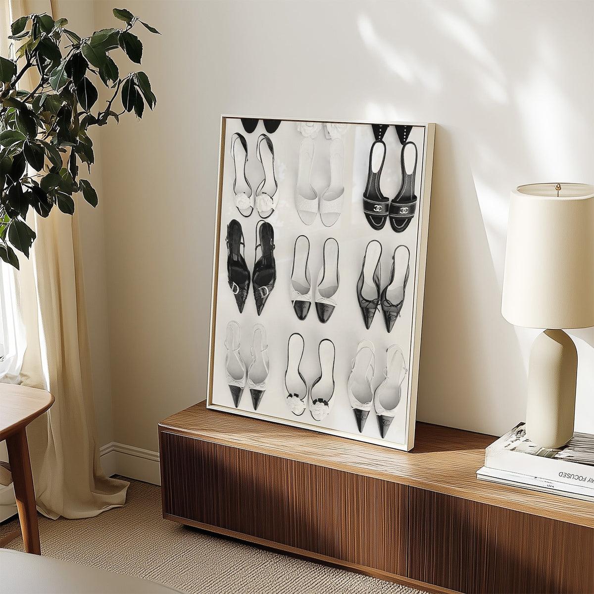 Nine pairs of mules and slingbacks in a grid print in a white frame on a walnut sideboard beside a ceramic lamp