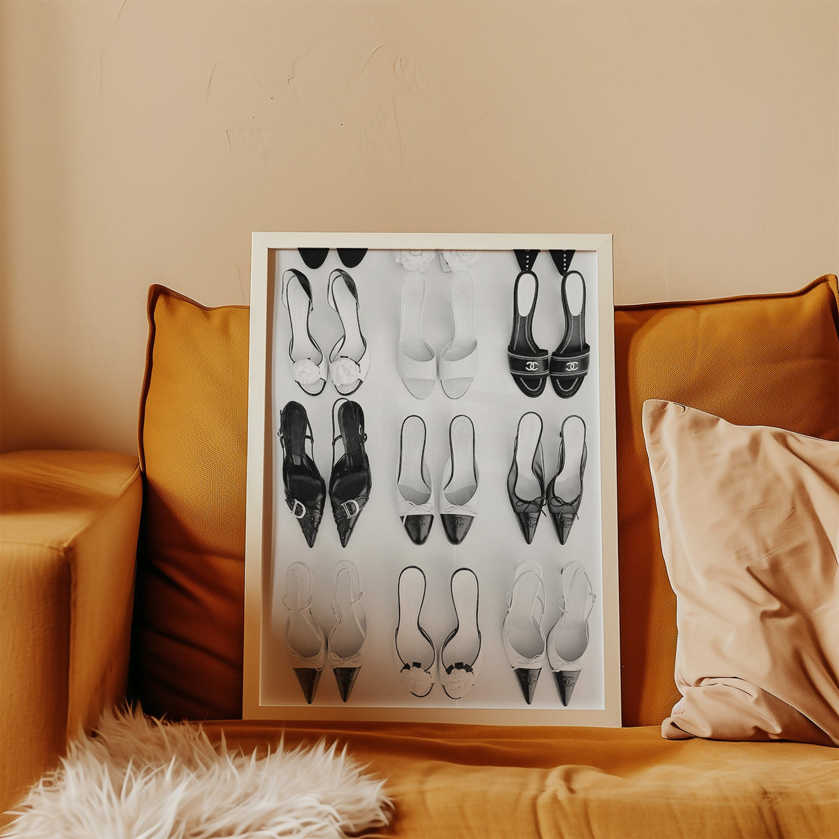 Nine pairs of mules and slingbacks in a grid print in a white frame leaning on a mustard velvet sofa