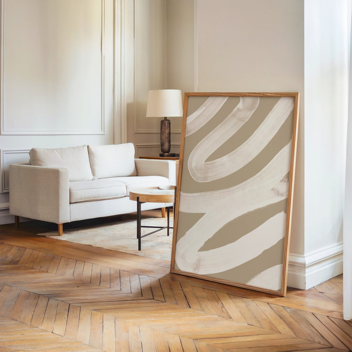 White brush zigzag on sand beige print in an oak frame leaning on a herringbone floor by a cream linen sofa