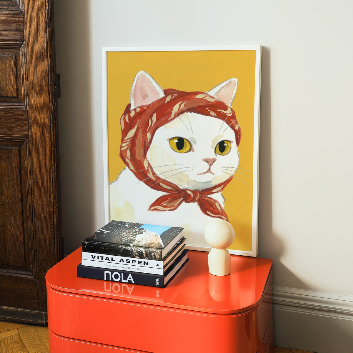 Cute cat portrait print in a white frame on a glossy orange cabinet with books