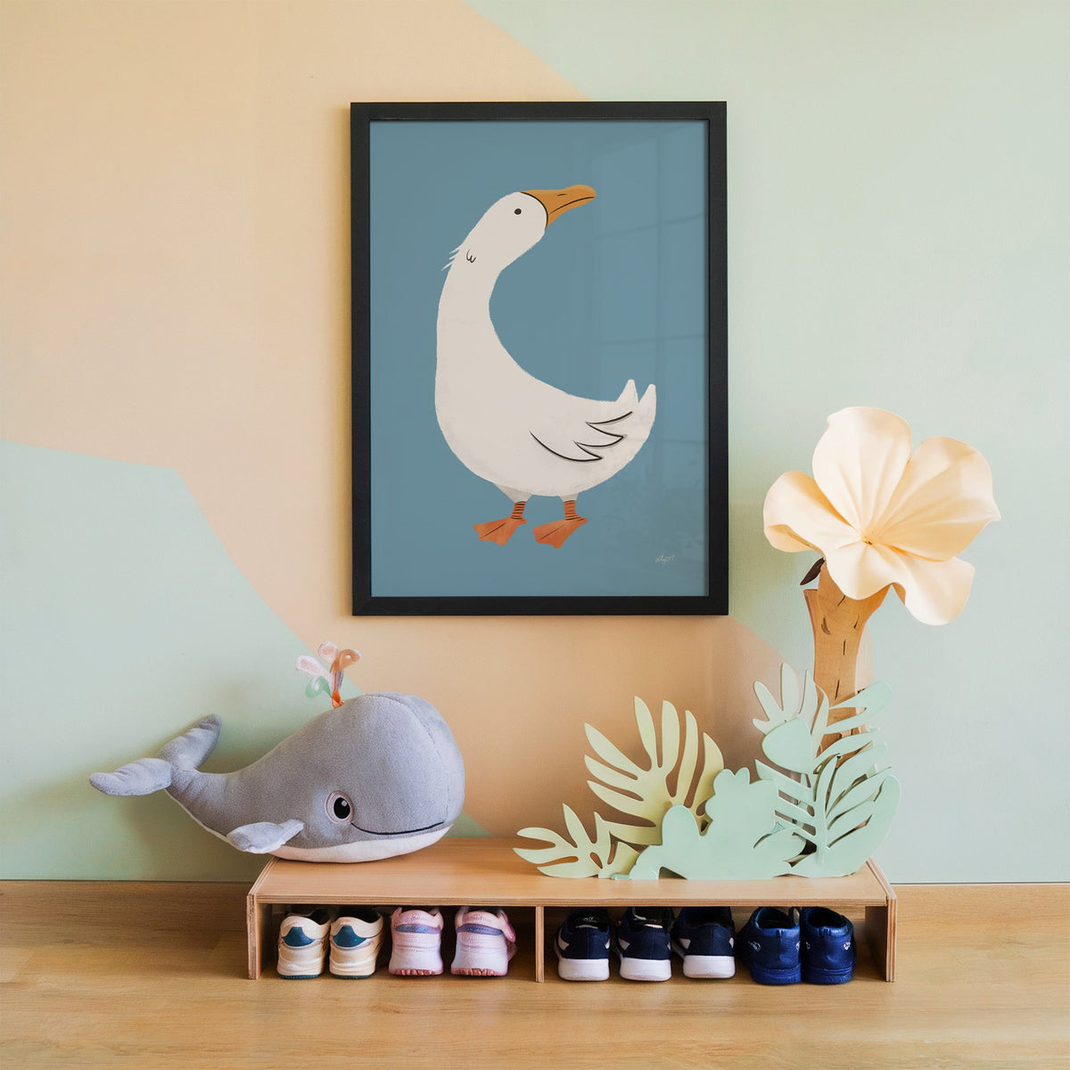 White goose on dusty blue nursery print in a black frame on a mint and peach wall above a whale plush