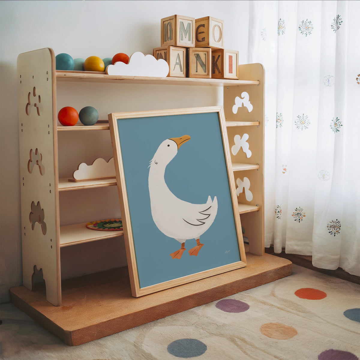 White goose on dusty blue nursery print in an oak frame leaning on a toy shelf with wooden letter blocks