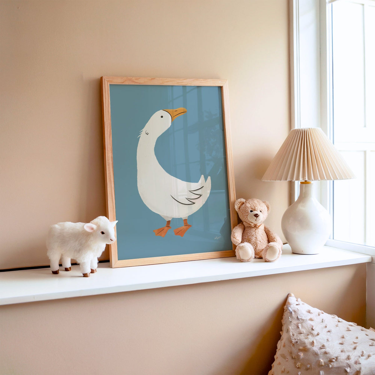 White goose on dusty blue nursery print in an oak frame on a window ledge with a toy lamb and teddy