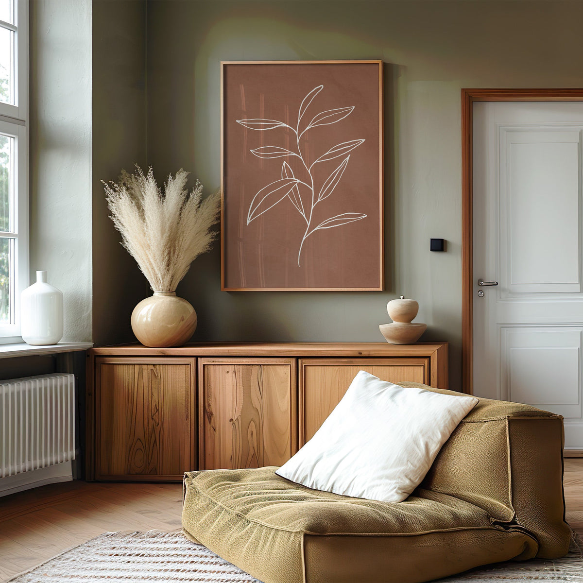 White line long leaf stem on terracotta print in an oak frame on an olive green wall above a wood sideboard with pampas