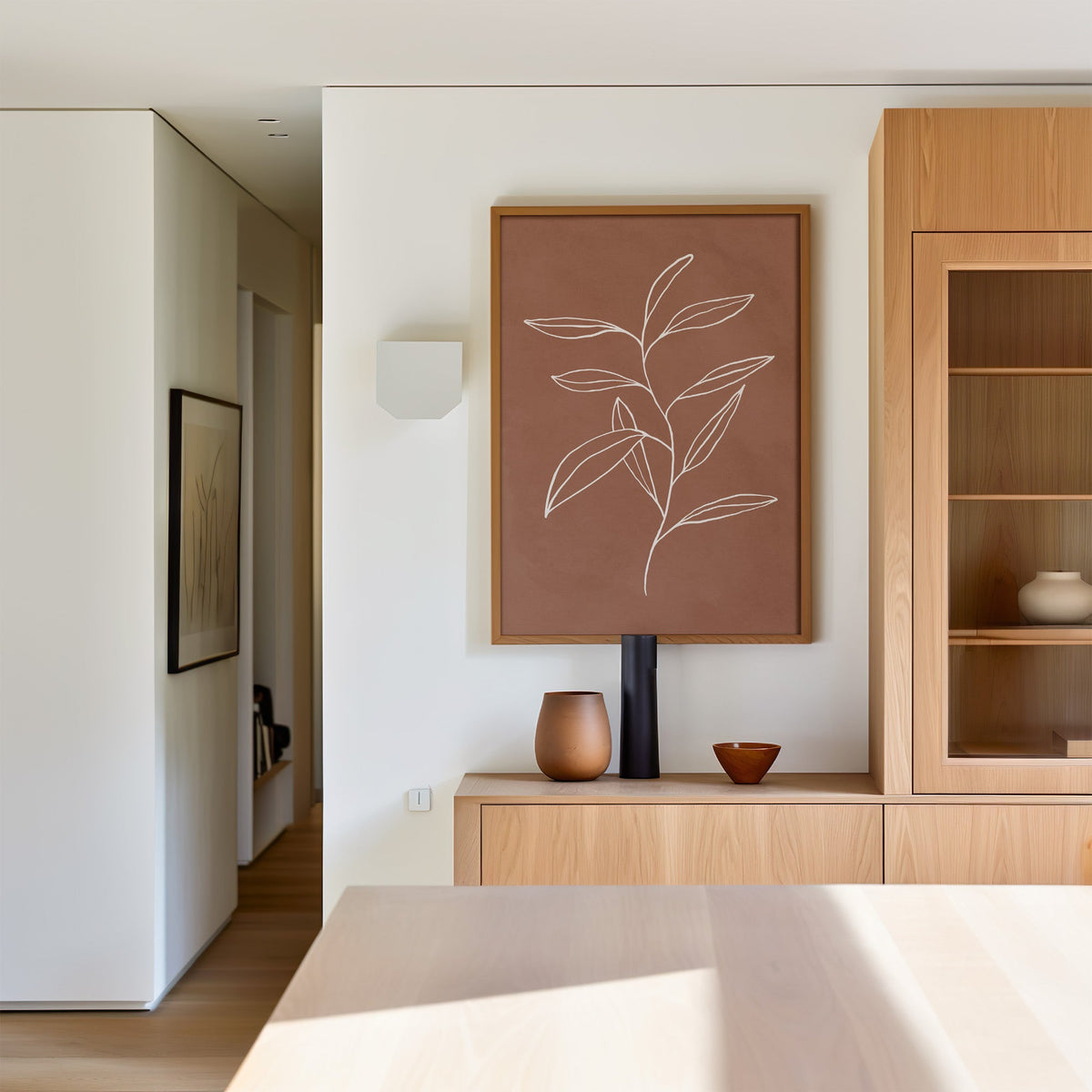White line long leaf stem on terracotta print in an oak frame above a light oak sideboard in a dining room