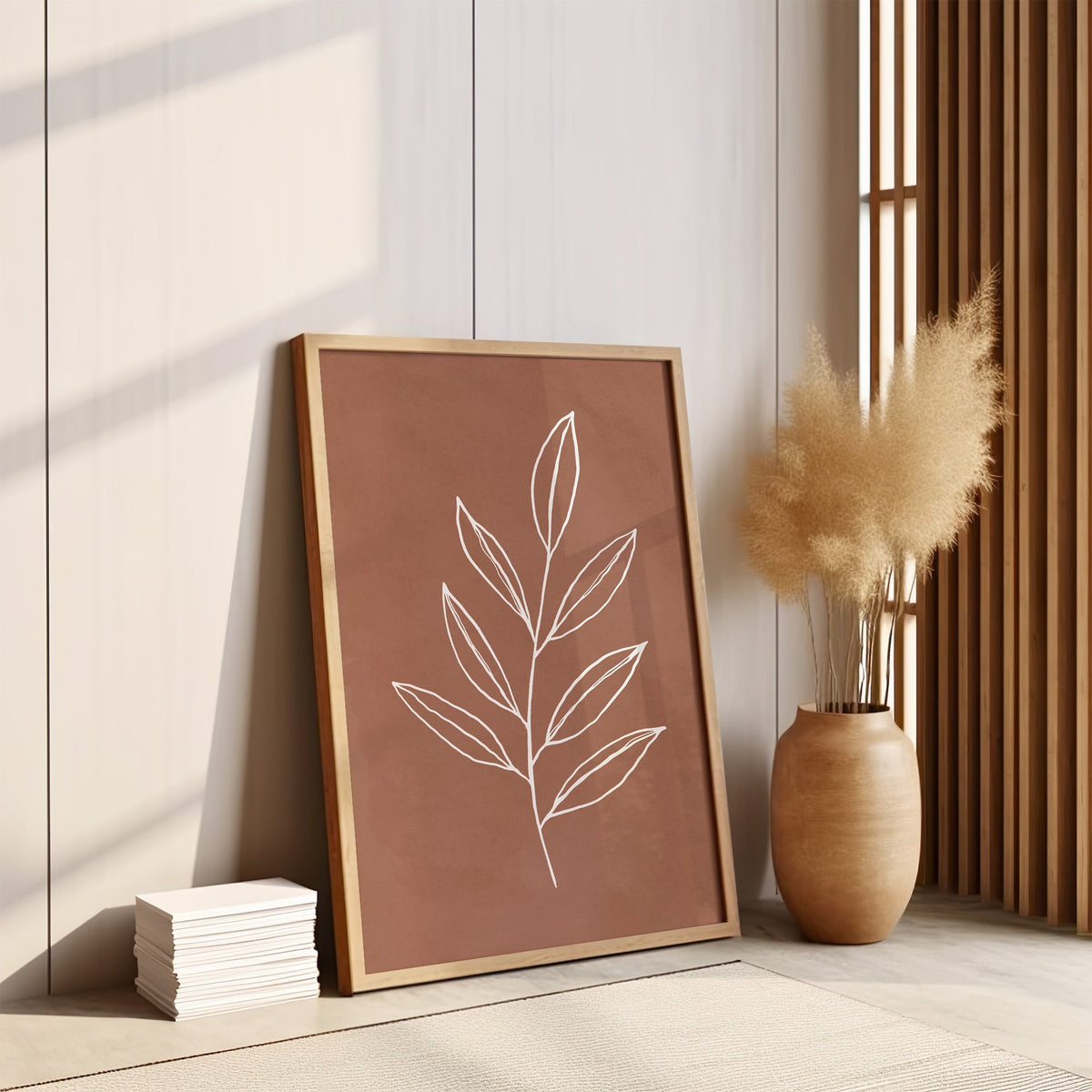 White line slender leaf sprig on terracotta print in an oak frame leaning on the floor by pampas grass and a wood slat screen