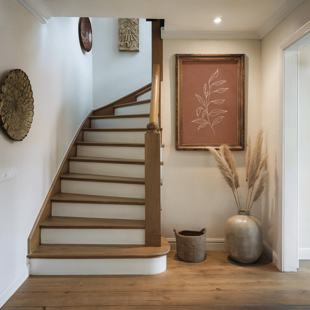 White line leafy sprig on terracotta print shown in a rustic wood frame in a hallway beside a wooden staircase