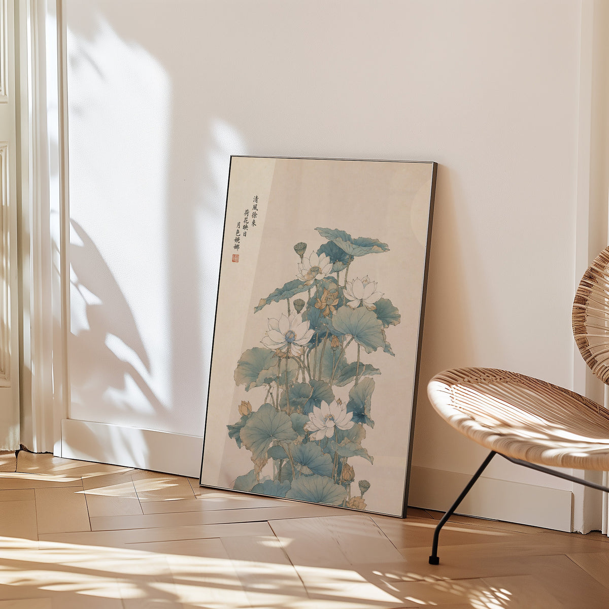 white lotus pond with verse print in a black frame leaning on a herringbone floor beside a woven rattan chair