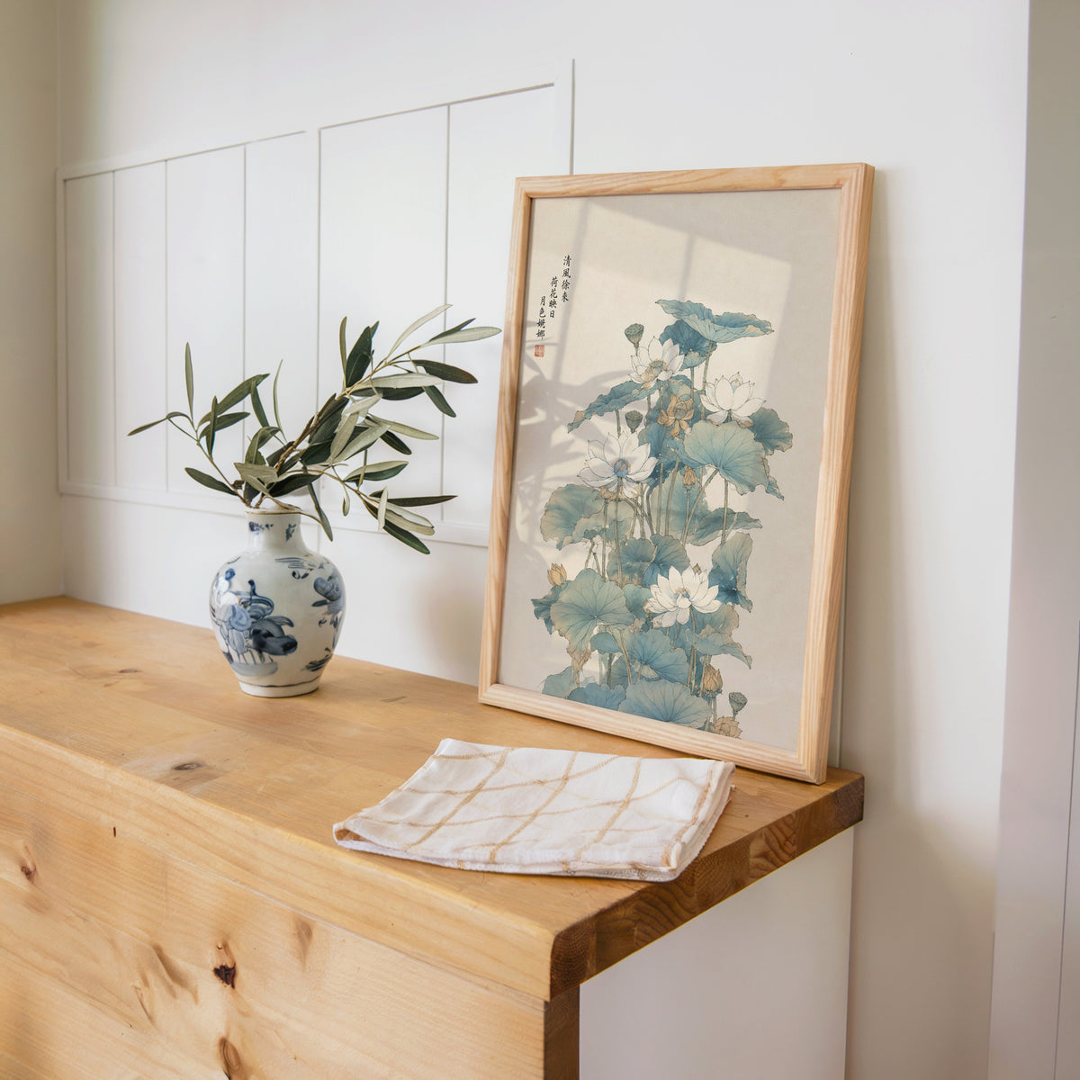 white lotus pond with verse print in a pine frame on a wooden counter beside a blue and white porcelain vase