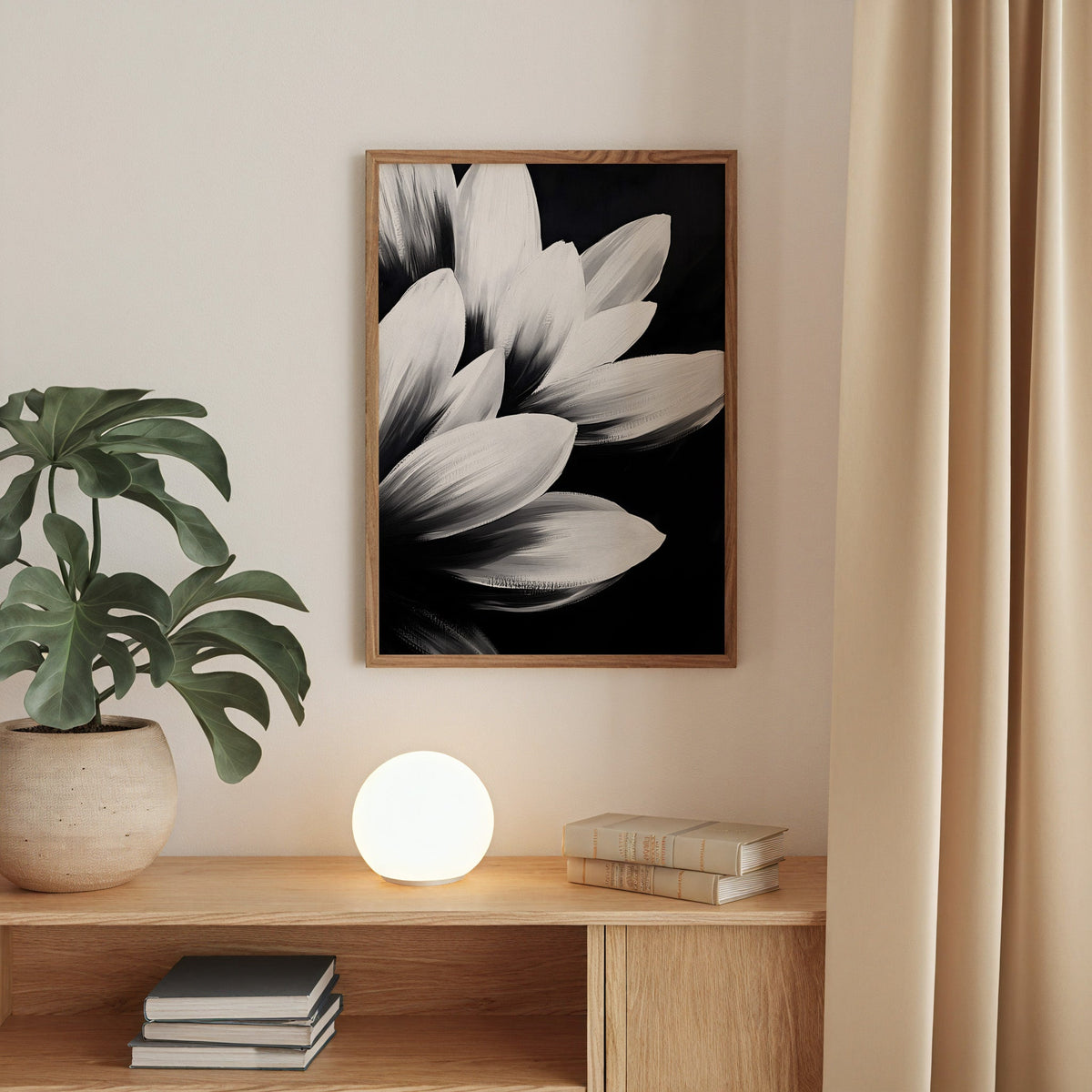 White petals on black background floral print in a walnut frame above an oak cabinet with a glowing globe lamp
