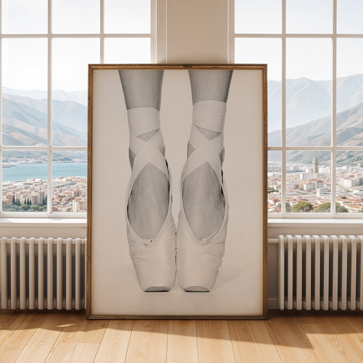 White pointe shoes with crossed ribbons close-up print shown in an antique gold frame by tall windows with a sea view