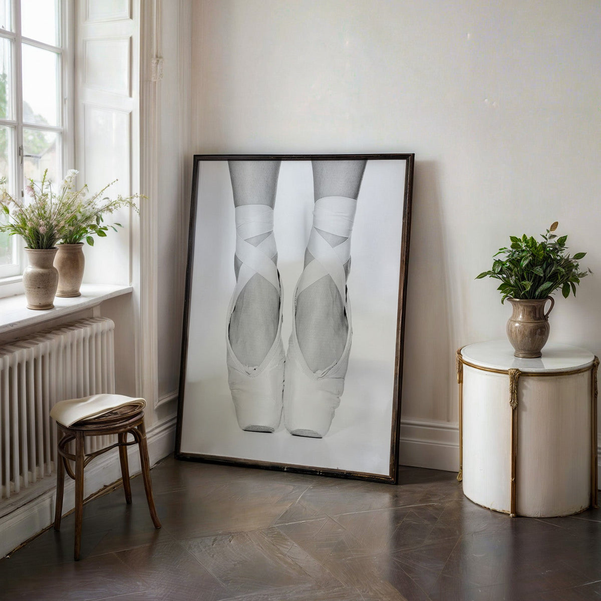 White pointe shoes with crossed ribbons close-up print in a black frame on a dark stone floor beside a white side table
