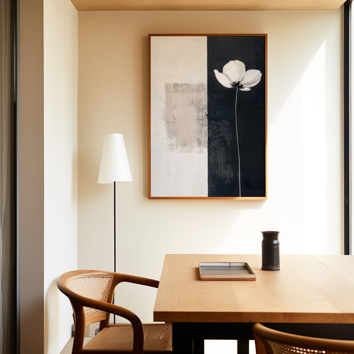 White flower on black and white split panel print in a slim oak frame above a dining table with a cane-back chair