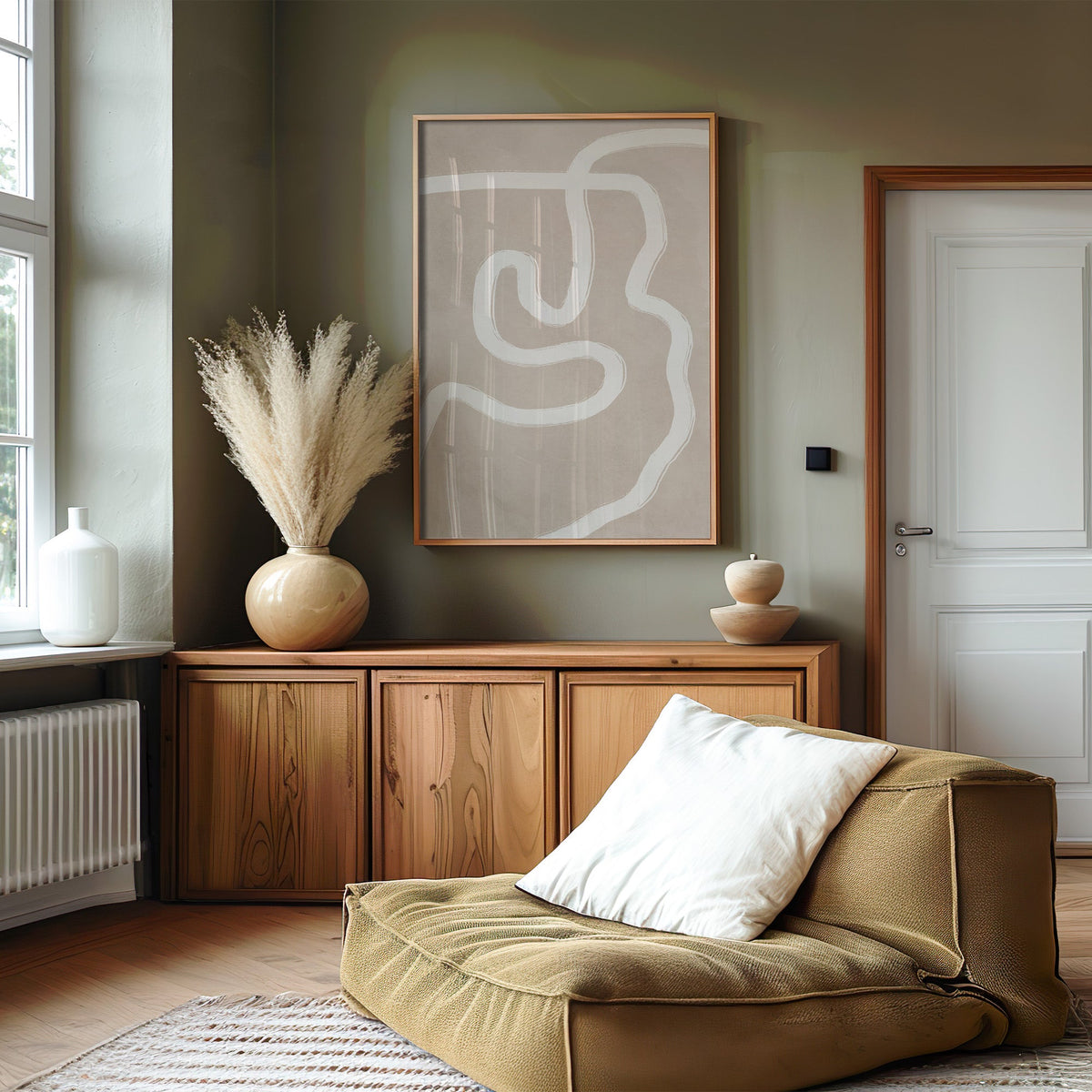 White squiggle brushstroke on taupe boho print in an oak frame on an olive green wall above a wood sideboard with pampas