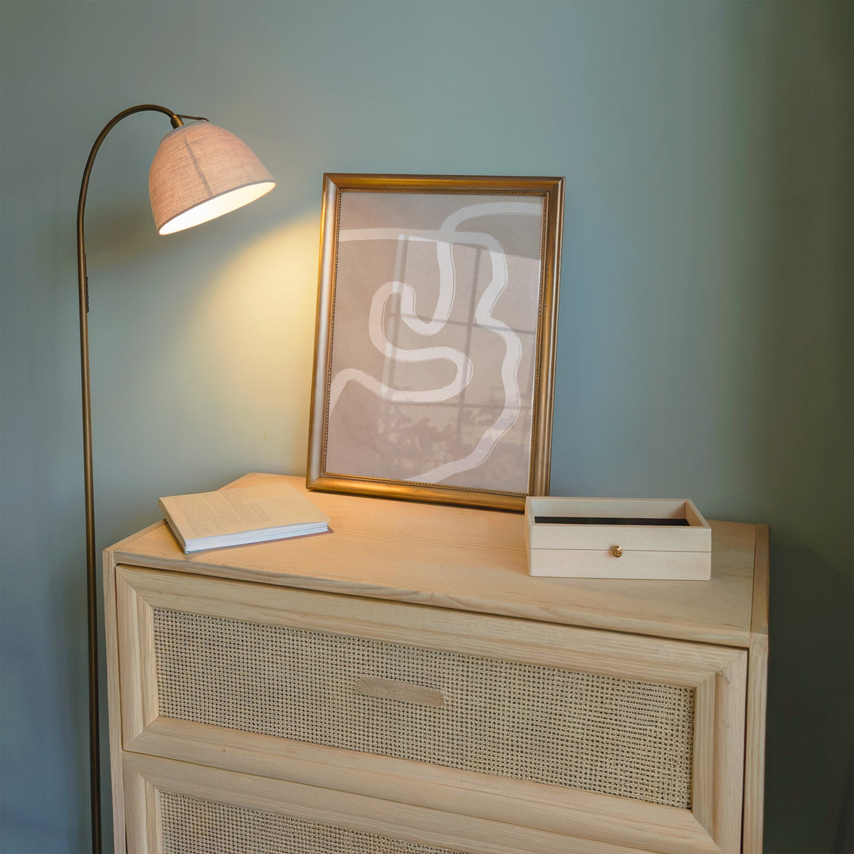 White squiggle brushstroke on taupe boho print shown in a gold frame on a cane dresser lit by a floor lamp