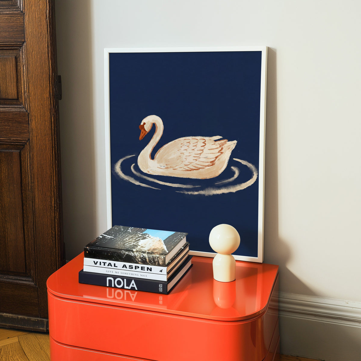Elegant swan print in a white frame on a glossy orange cabinet with books