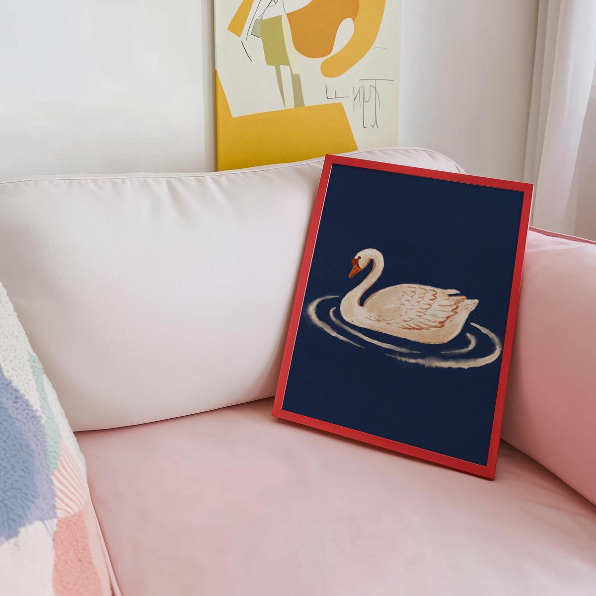 Cream swan painting print shown in a red frame leaning on a blush pink sofa