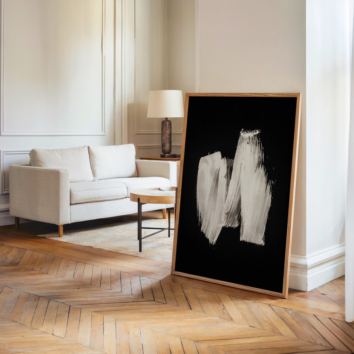White zigzag brushstroke on black print in an oak frame leaning on a herringbone floor by a cream linen sofa