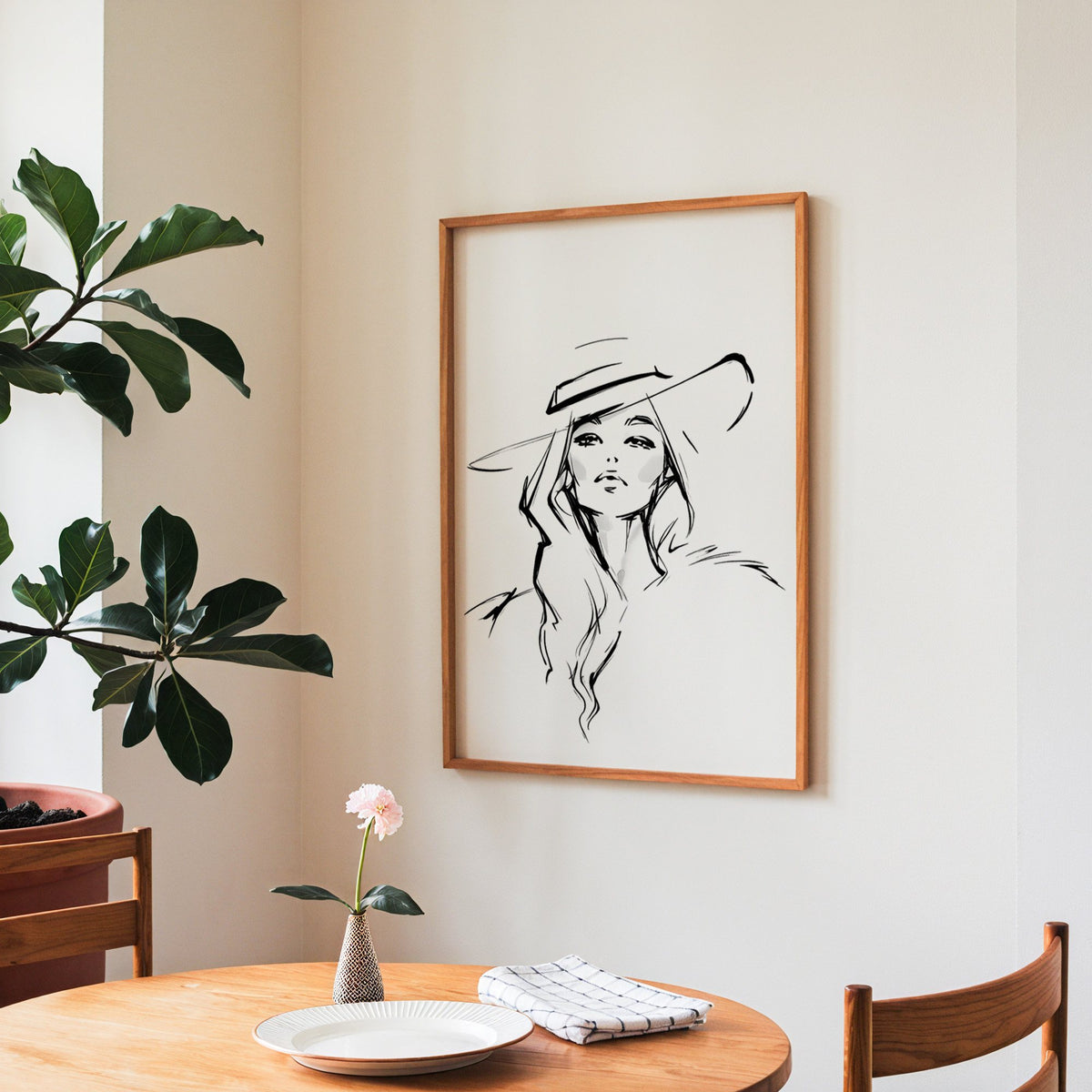 Line sketch of woman in wide brim hat print in a teak frame above a round wooden dining table