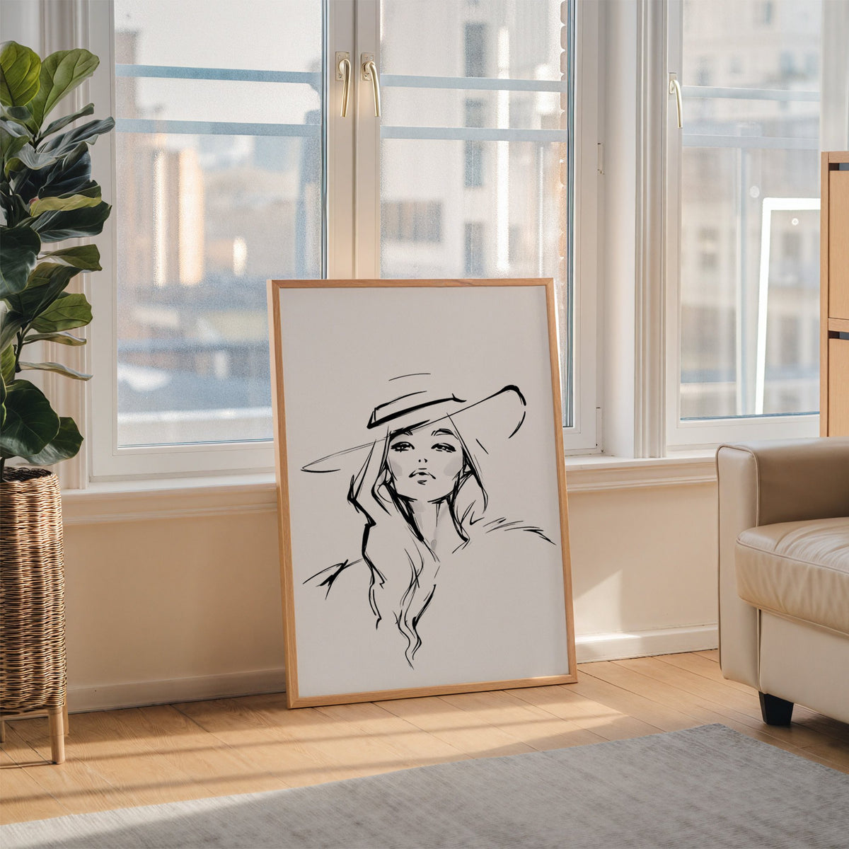 Line sketch of woman in wide brim hat print in an oak frame leaning on the floor beside a fiddle leaf fig