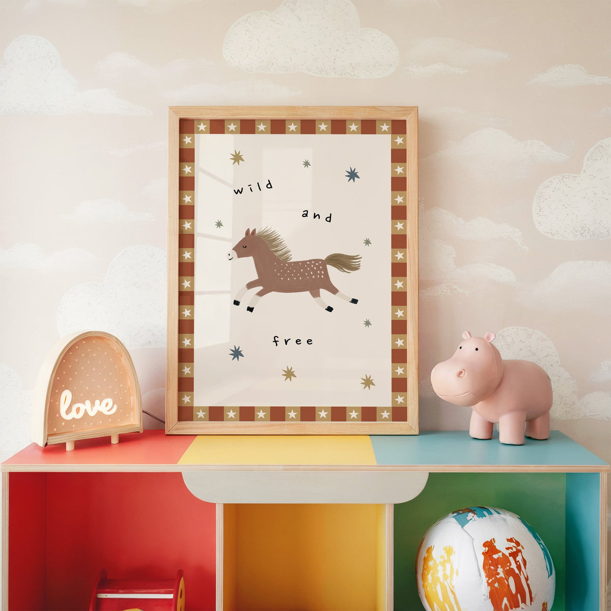 Wild and free pony nursery print in an oak frame on a rainbow toy shelf against cloud wallpaper